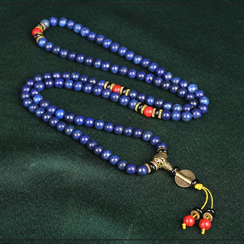 Long lapis lazuli prayer mala necklace coiled on silk fabric, showing full strand with gold hardware and decorative red tassel pendant