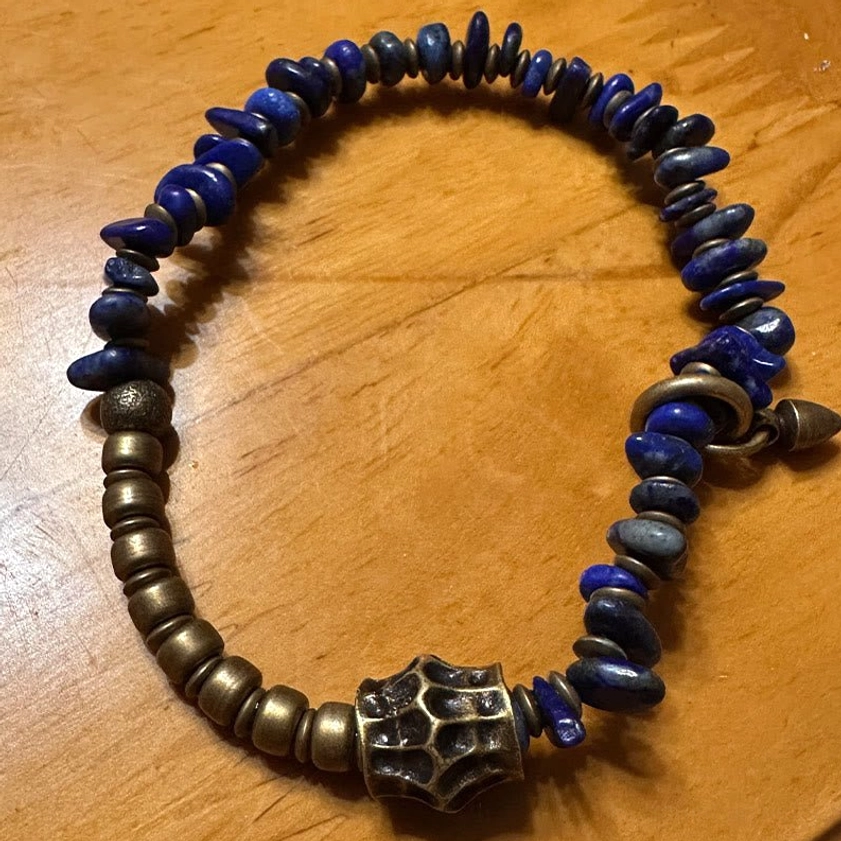 Lapis lazuli and bronze Buddhist bracelet with large carved metal focal bead and spacer accents on light wooden table