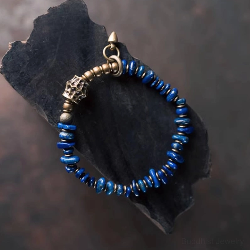 Close-up side view of lapis lazuli chip beaded bracelet featuring ornate carved metal spacer beads on rustic wood slab