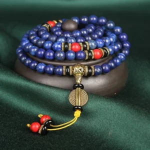 Lapis lazuli 108 bead mala bracelet with gold metal accents and red turquoise tassel, displayed on wooden base with dark green fabric