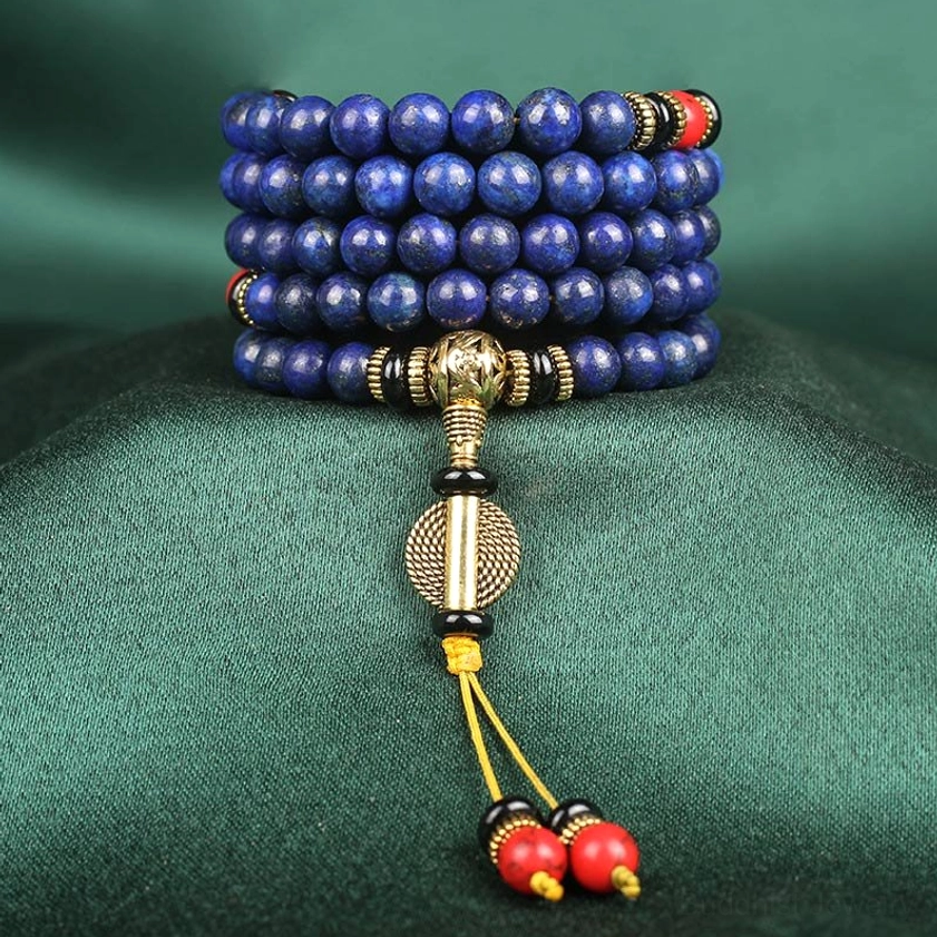 Multiple lapis lazuli prayer mala bracelets stacked and coiled with ornate gold pendant and red tassel charms, front close-up view