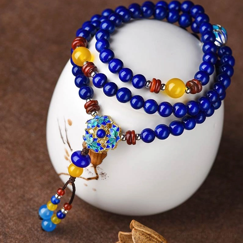 Double-wrap Lapis Lazuli mala bracelet with yellow and brown accent beads, featuring blue enamel flower pendant on white ceramic display