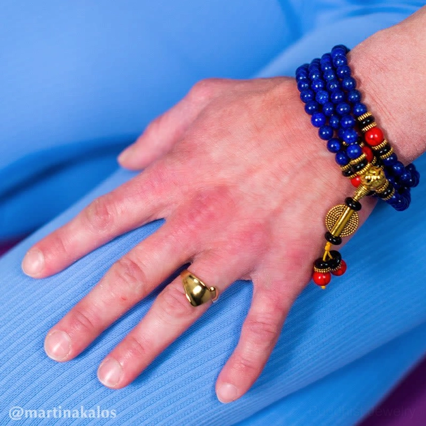 Close-up hand view of lapis lazuli mala bracelet worn with blue athletic wear, showing stone beads gold metal charm and red accent beads