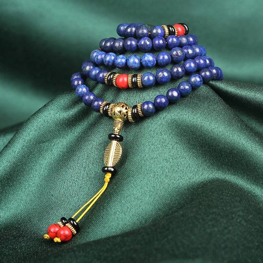 Lapis lazuli mala bracelet stacked beads close-up with gold metal spacer and red tassel charm on dark green background