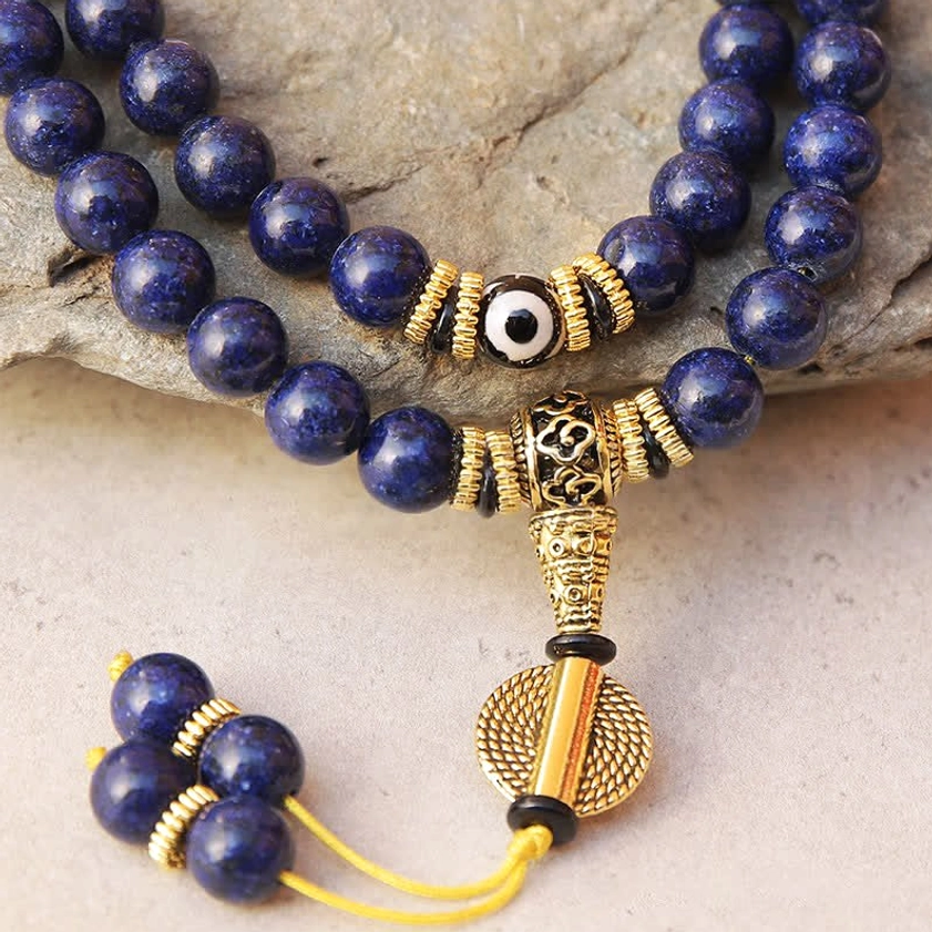 Close-up detail of lapis lazuli prayer mala beads showing natural stone texture and evil eye Dzi bead with intricate gold hardware