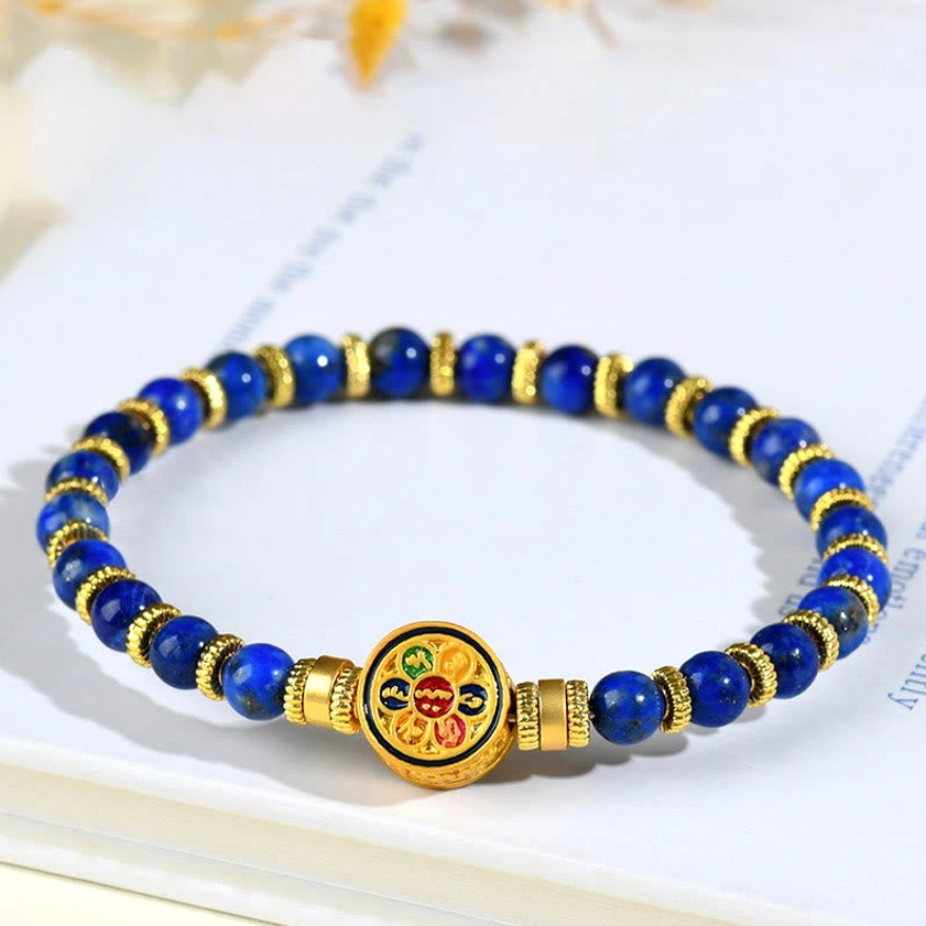 Lapis lazuli om mani padme hum bracelet with blue stone beads and gold accents on office desk