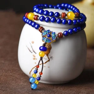 Multi-layer Lapis Lazuli and Yellow Agate mala bracelet with blue enamel flower pendant, displayed on white ceramic jar for jewelry photography