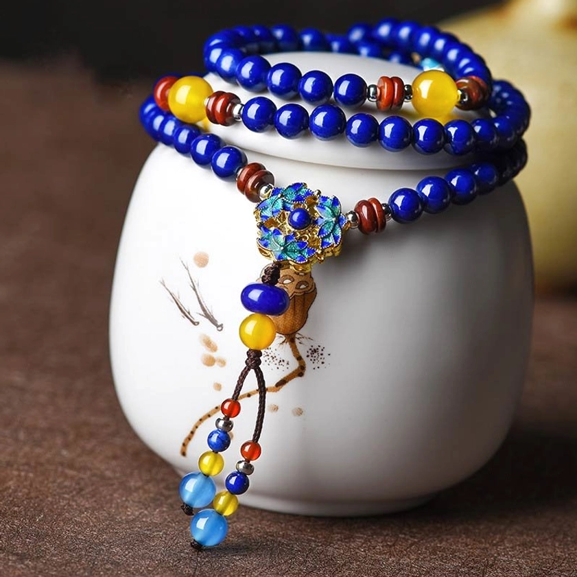 Multi-layer Lapis Lazuli and Yellow Agate mala bracelet with blue enamel flower pendant, displayed on white ceramic jar for jewelry photography