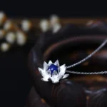 Lapis lazuli lotus flower sterling silver necklace pendant with 3D blooming design, deep blue gemstone center, displayed on wooden surface with dried flowers