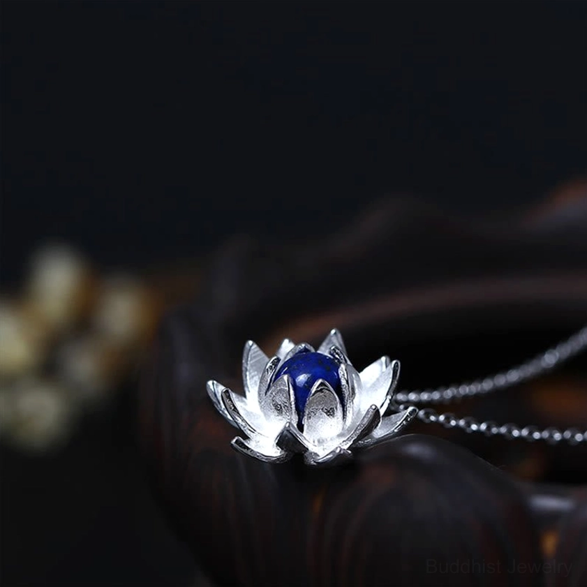 Lapis lazuli lotus pendant necklace close-up, three-quarter angle shot highlighting intricate silver petals and deep blue gemstone with blurred floral background