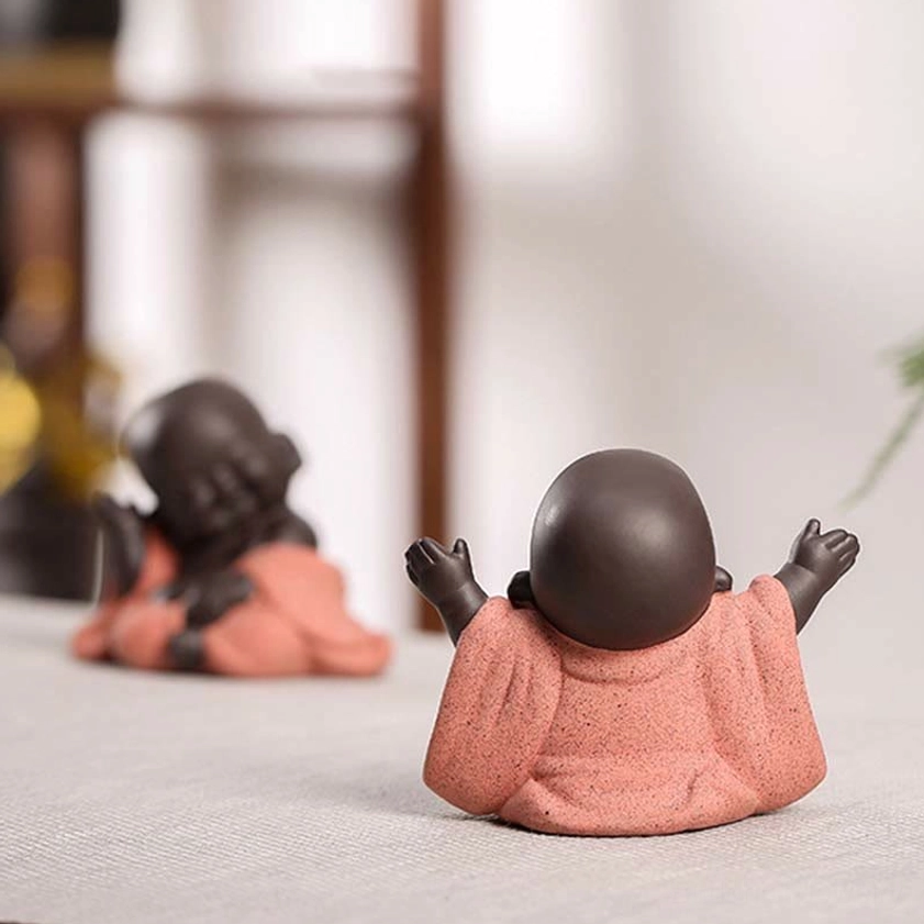 Baby Buddha statue rear view showing smooth dark brown bald head and pink robe detail, handmade purple clay