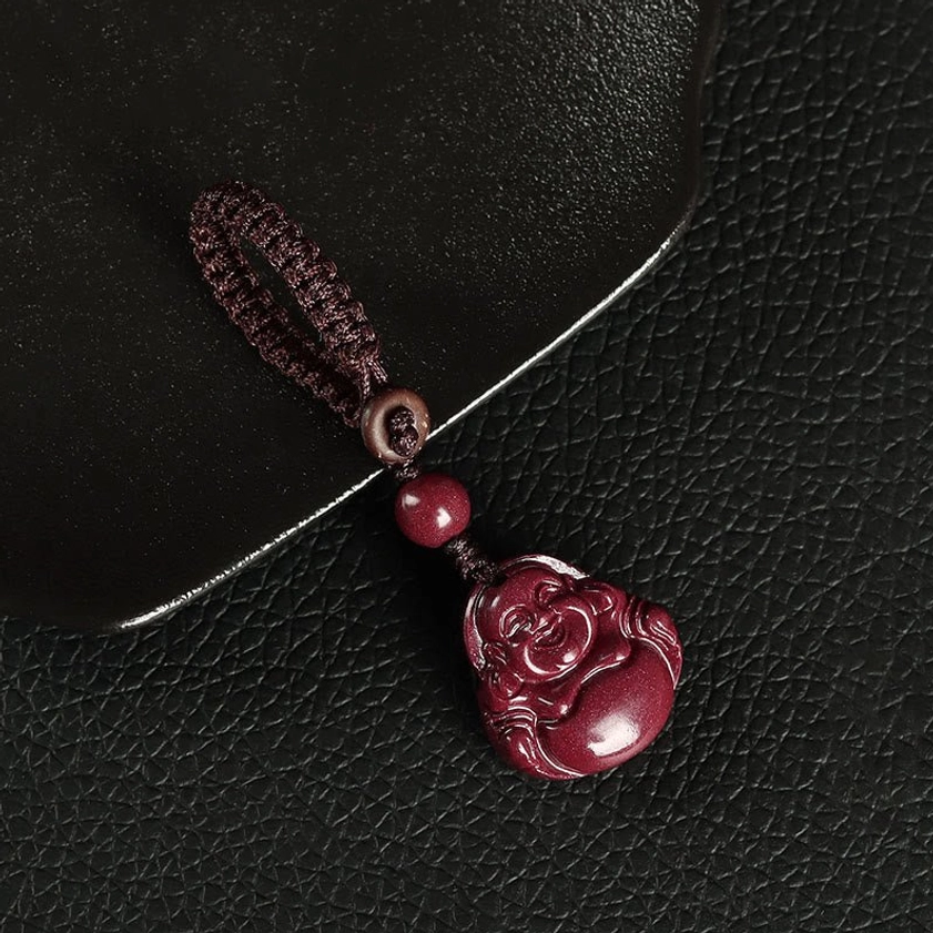 Brown Laughing Buddha cinnabar keychain pendant with wooden ring detail on black leather background