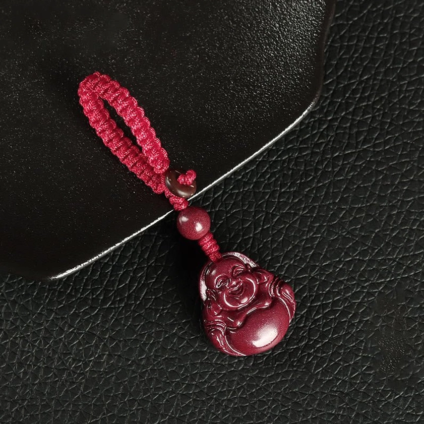 Red woven Laughing Buddha cinnabar keychain pendant with knotted rope design on black tray flat lay