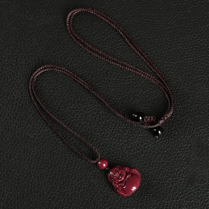 Brown braided rope Laughing Buddha cinnabar necklace pendant with decorative black beads on leather background flat lay