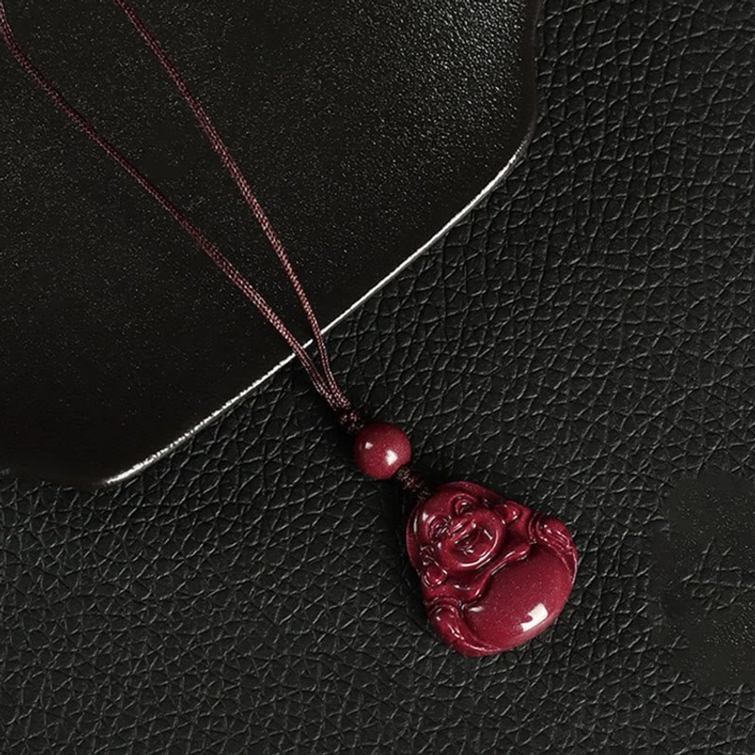 Dark brown braided Laughing Buddha cinnabar phone charm pendant with polished carving detail on black tray
