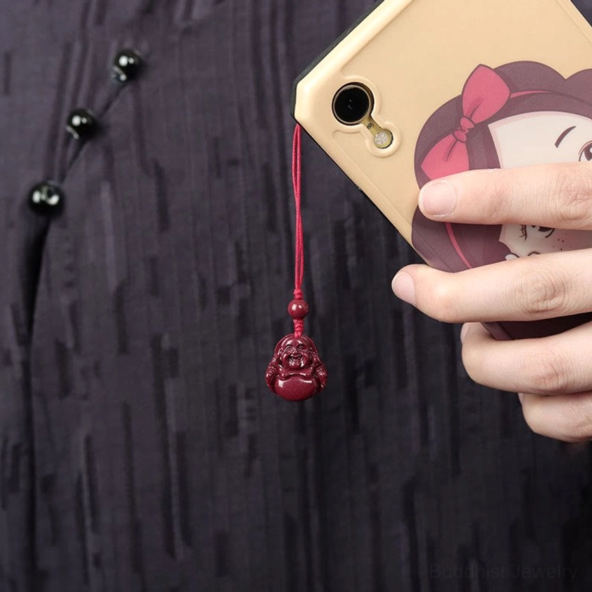 Red Laughing Buddha cinnabar phone charm hanging on smartphone camera demonstrating everyday spiritual protection use
