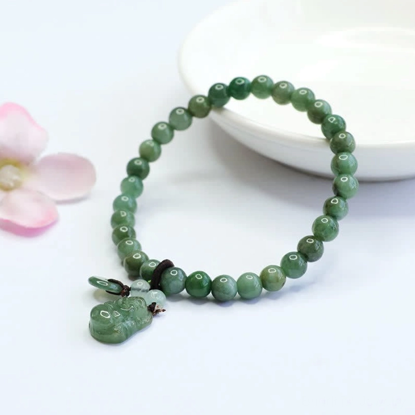 Laughing Buddha Cyan Jade Buddha bracelet paired with white ceramic bowl and pink flowers on soft background