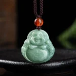 Laughing Buddha cyan jade pendant necklace displayed on black ceramic tray, showing front view with intricate carved smiling Buddha face