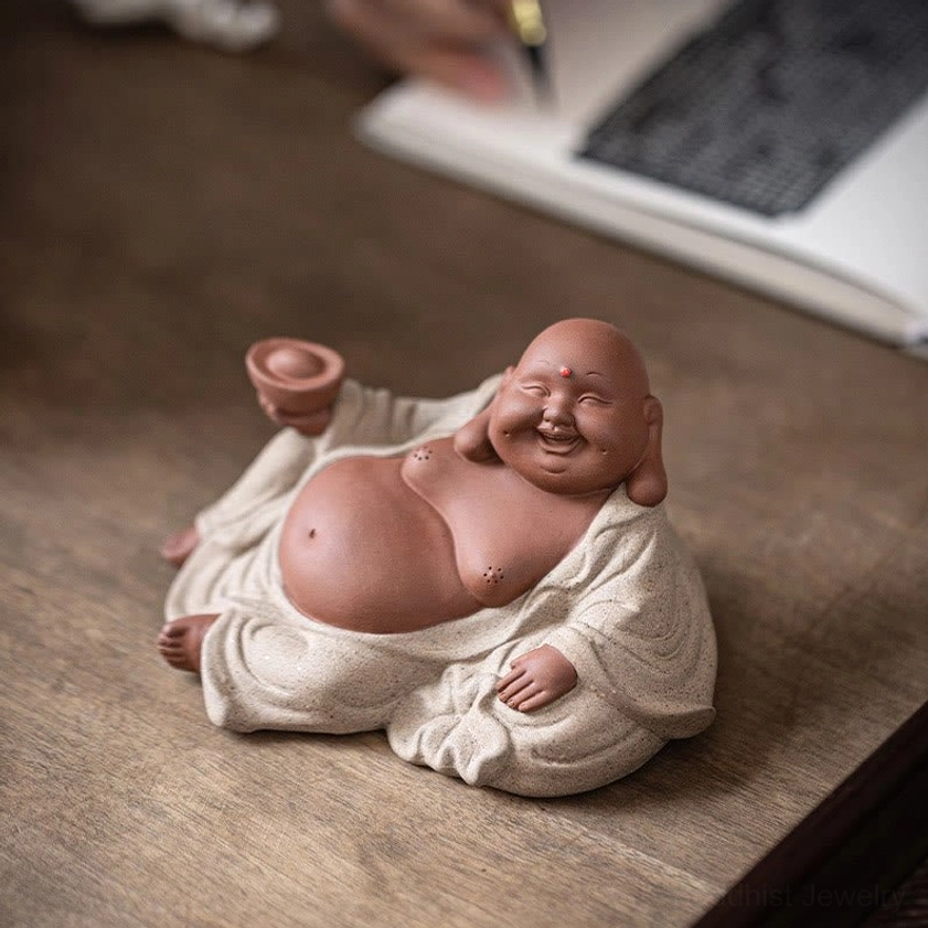 Laughing Buddha holding wealth ingot on wooden desk with notebook, front three-quarter view, smiling face, abundance symbol