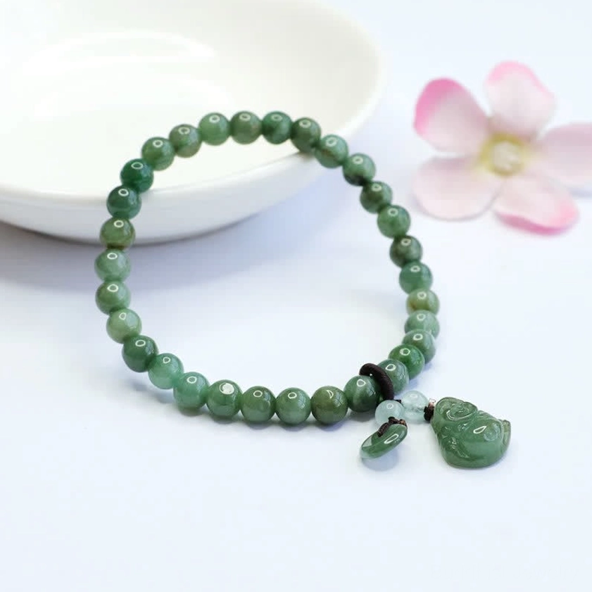 Laughing Buddha Buddhist jade bracelet with dark knot fastener next to white ceramic bowl and pink flowers on neutral background