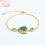 Green jade Laughing Buddha bracelet with zircon crystals and gold-plated chain on pink floral background - prosperity bracelet for good luck