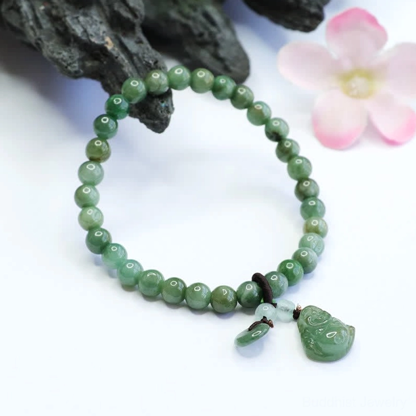 Cyan Jade Laughing Buddha healing bracelet displayed with pink flowers and dark mineral stones, showing intricate Buddha pendant charm detail