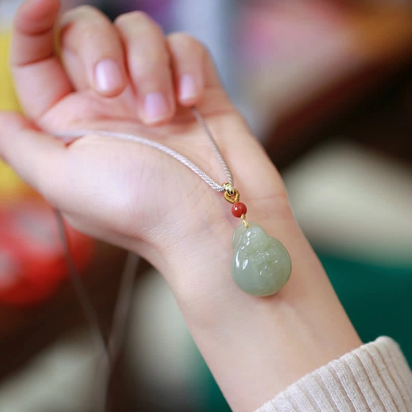 Laughing Buddha jade necklace worn on wrist with adjustable braided cord, styled with beige knit sweater