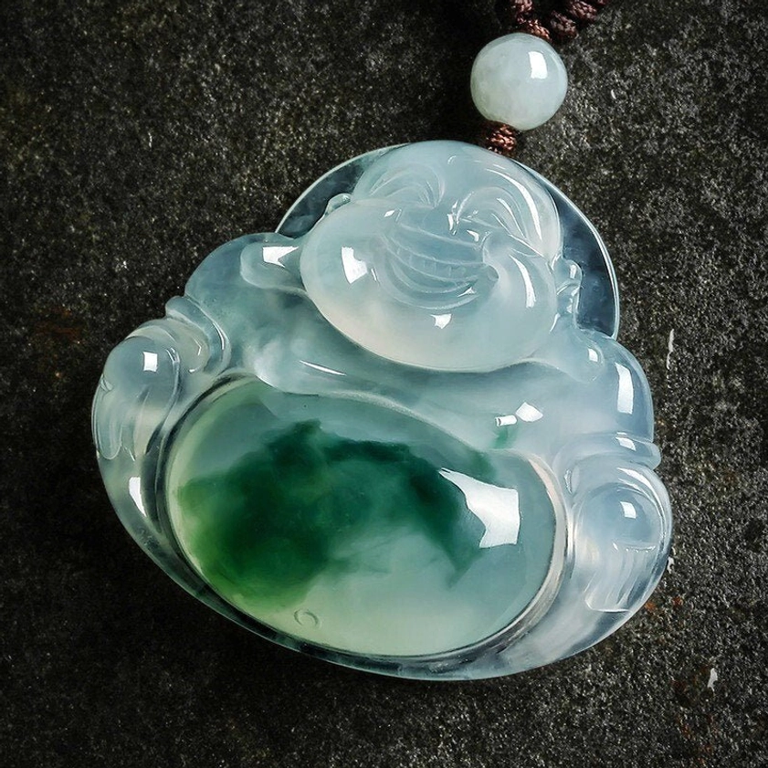 Translucent cyan jade Buddhist necklace pendant featuring Maitreya Buddha carving with intricate green belly patch detail, captured in angled overhead view