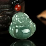 Green jade Laughing Buddha pendant with red bead and black braided cord on wooden background, front view showing smiling carved Buddha face