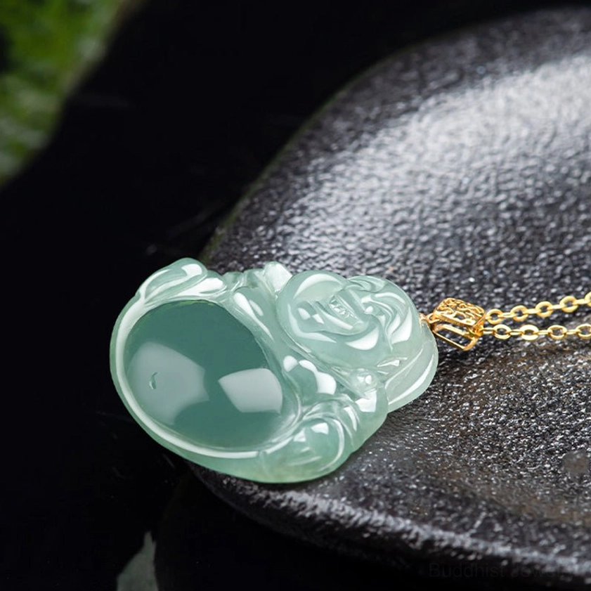 Laughing Buddha jade pendant with gold chain displayed flat on black stone plate overhead view
