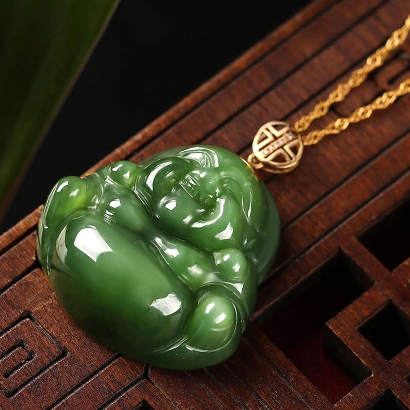 Overhead view of laughing Buddha jade pendant lying on wooden lattice display with gold chain and longevity emblem