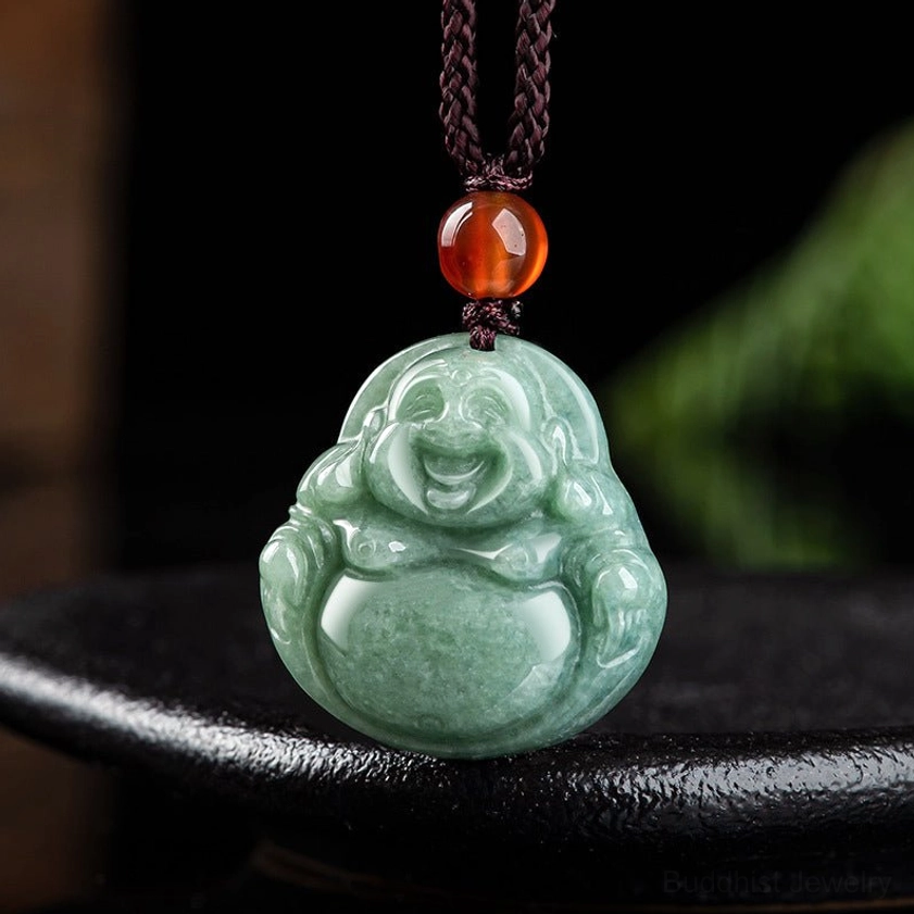 Top view of handmade cyan jade Buddha pendant on brown twisted rope with amber bead, displaying polished stone surface
