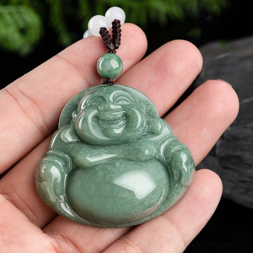 Cyan jade laughing Buddha pendant held in hand showing scale and size, with green foliage background