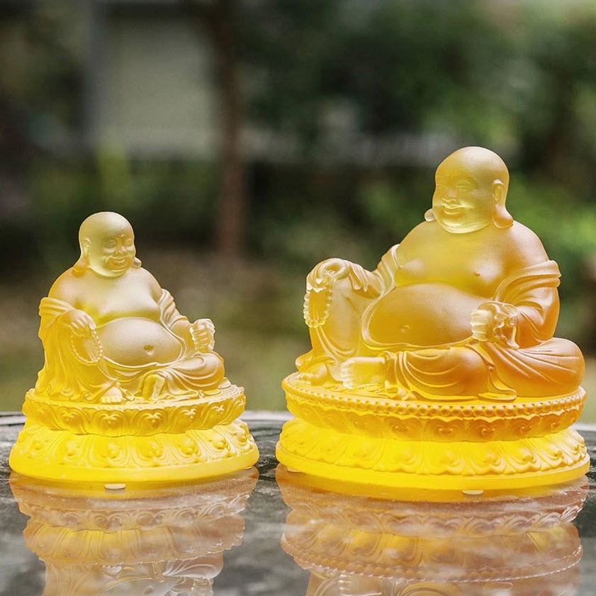 Two sizes of Laughing Buddha Liuli crystal statues comparison side-by-side outdoor setting warm amber glass seated lotus throne design