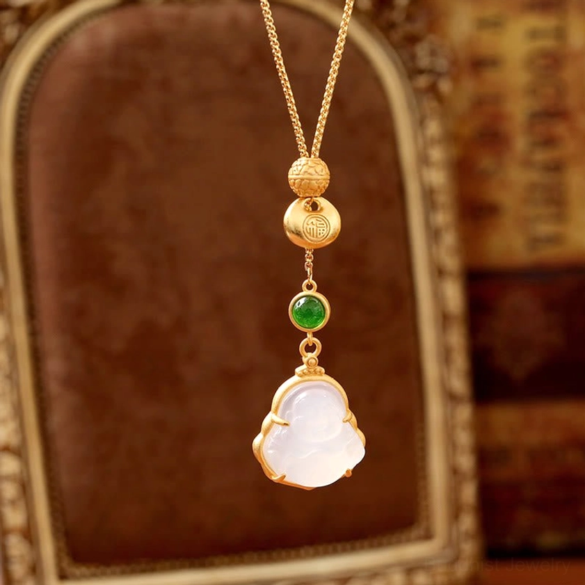 Buddhist necklace pendant front view with polished white Laughing Buddha charm, green round stone, and stacked engraved gold beads against vintage gold frame backdrop