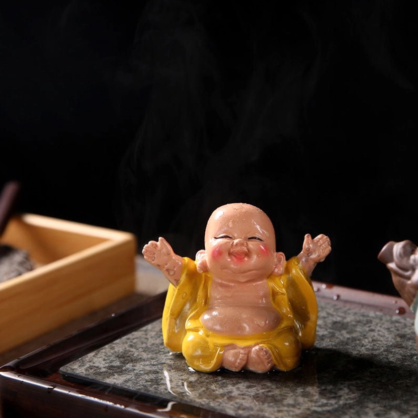 Low angle front view of laughing Buddha tea pet in light yellow original color on wooden tea tray, smiling monk figurine