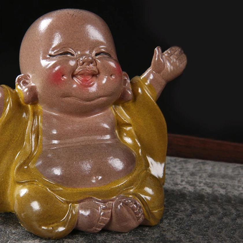 Left side view of laughing Buddha resin pet with raised hand gesture, matte brown torso, yellow robe shoulders