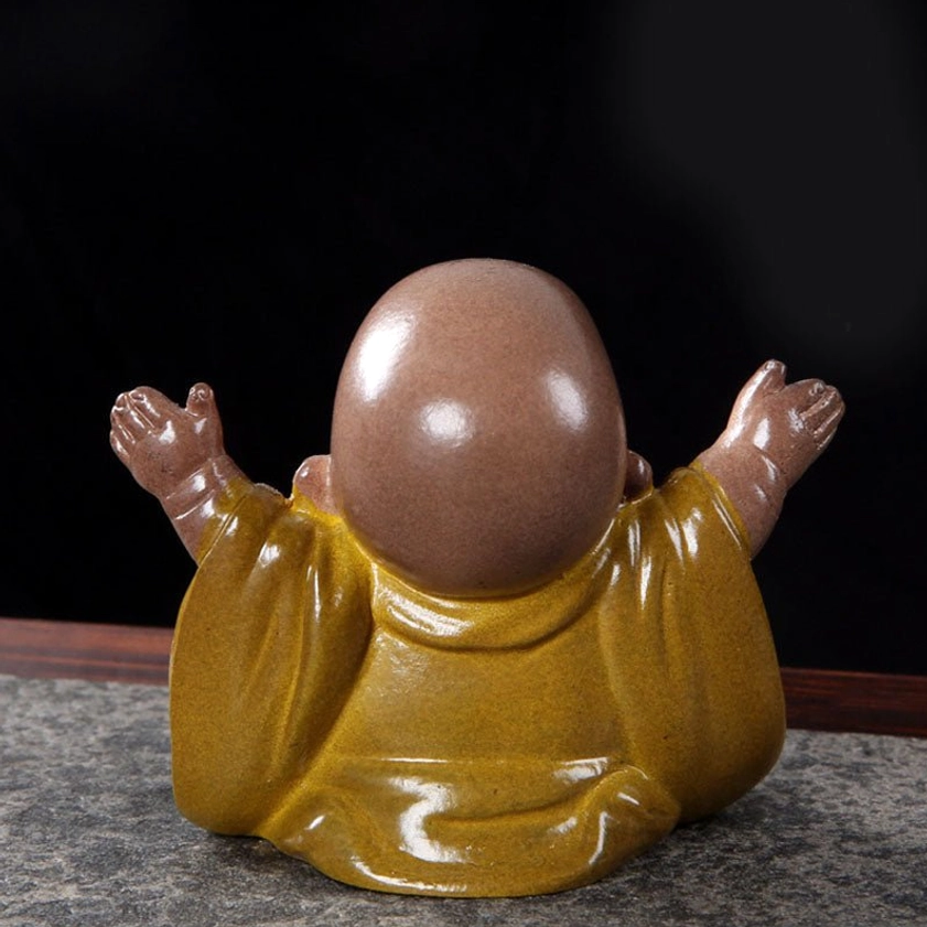 Rear view of handmade laughing Buddha showing smooth round head, yellow robe, and back profile of the figurine