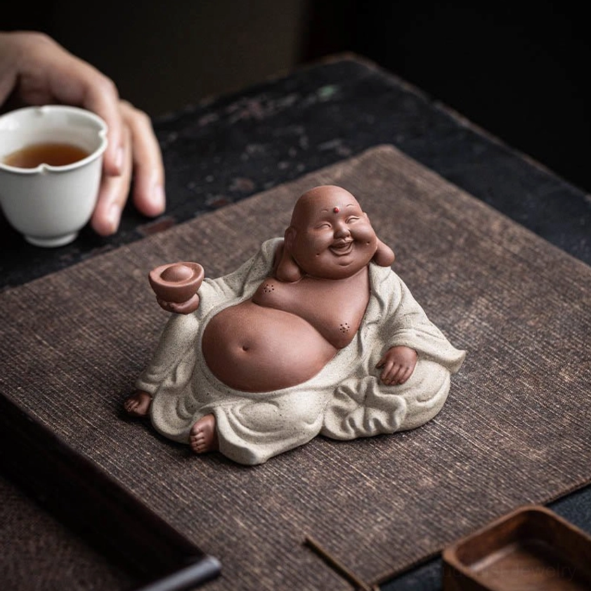 Laughing Buddha tea pet with relaxed smiling posture on tea table with tea set, purple clay, meditation and mindfulness