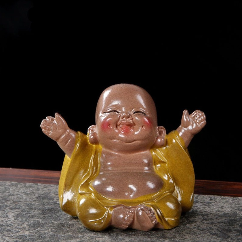 Front view of resin laughing Buddha tea pet with raised arms, blushed cheeks, matte brown skin tone on marble surface