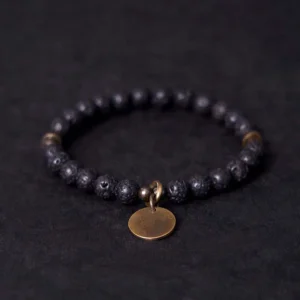 Lava rock beads bracelet with antique bronze copper pendant, three-quarter overhead view showing matte black porous volcanic beads and metal disc charm