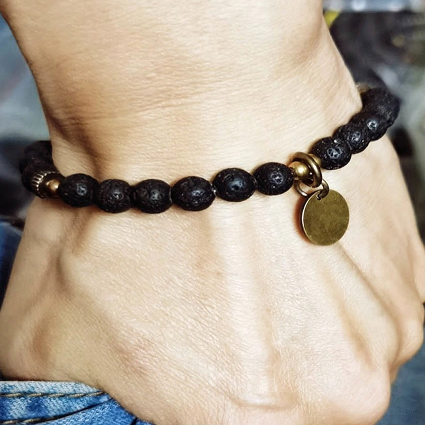 Real person wearing lava rock beads Buddhist bracelet on wrist, demonstrating fit and styling with matte black beads and copper pendant