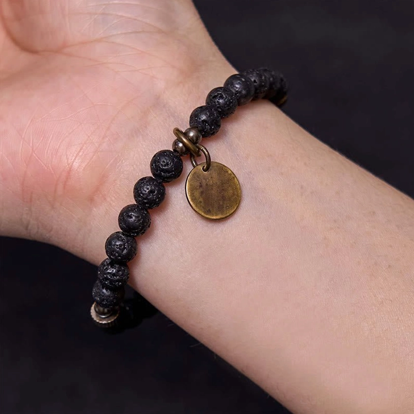 Close-up wrist-worn lava rock beads bracelet showing pendant and volcanic bead texture, highlighting comfort fit and antique bronze charm
