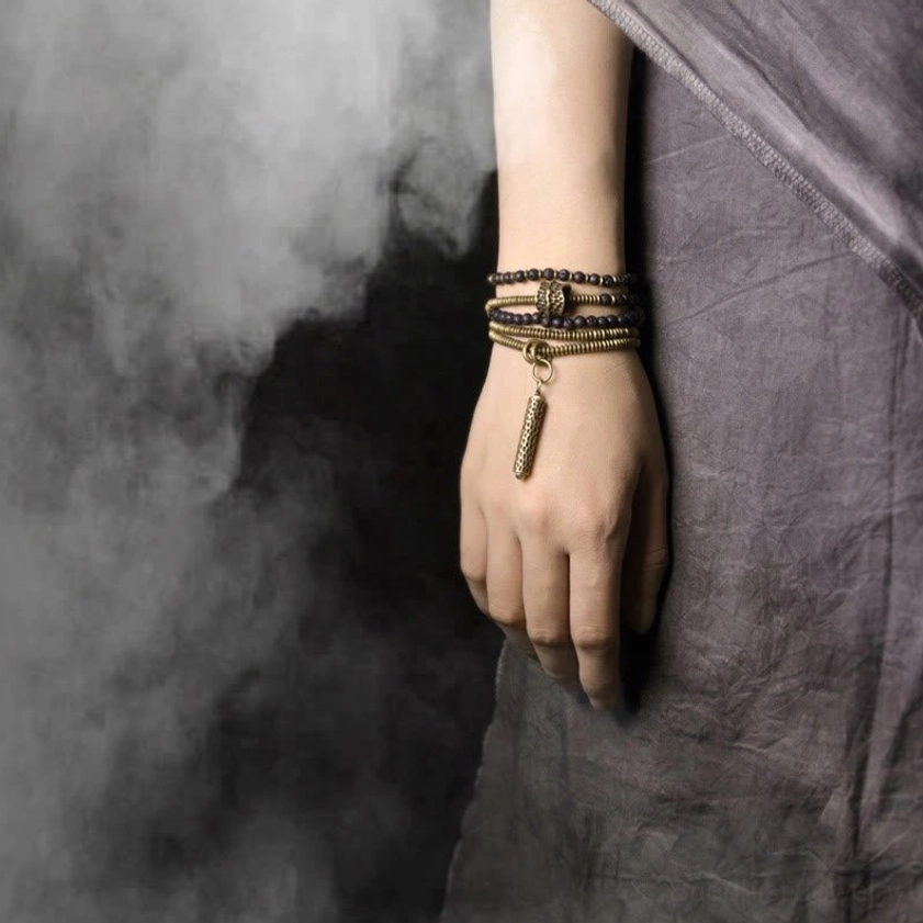 Worn lava rock and brass multilayered bracelet set on wrist - side close-up with dangling tassel