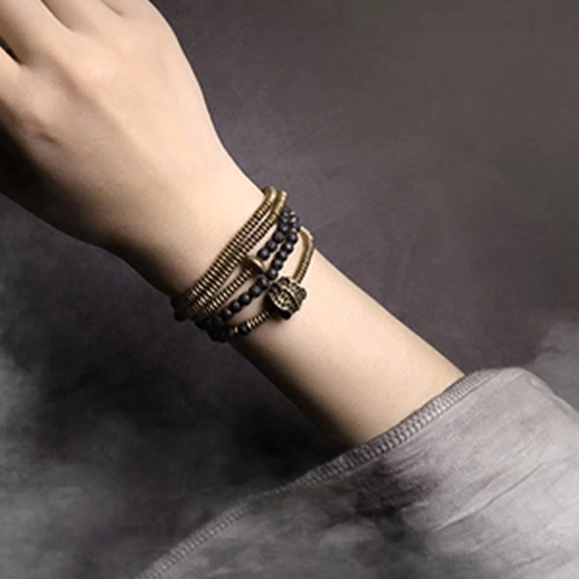 Stacked lava rock and brass healing bracelet layers on wrist - flat lay close-up detail view