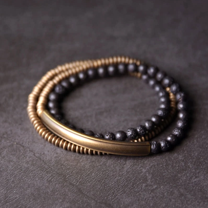 Vintage lava rock copper grounding bracelet flat lay top view with antique brass beads and black volcanic stone on dark texture background