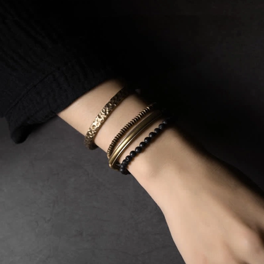 Mixed antique copper and lava rock beaded bracelets stacked on hand showing engraved brass bands and grounding stone details