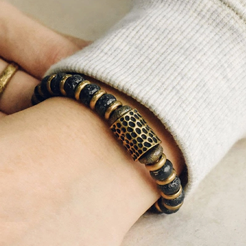 Decorative hammered copper bead on lava rock bracelet close-up worn on inner wrist with sweater sleeve