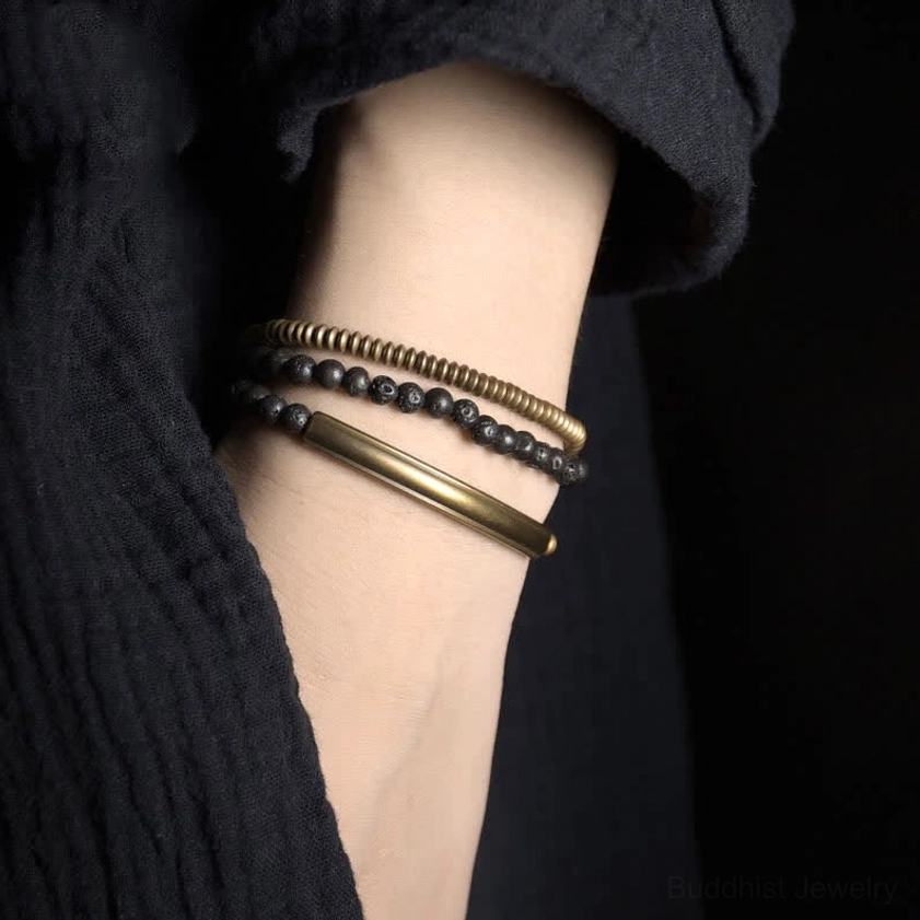 Layered lava rock copper bracelets worn on wrist close-up side view showing antique brass metal tubes and black lava beads