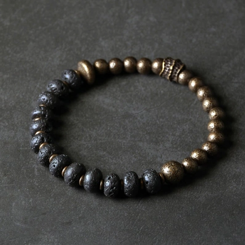 Full view of complete lava rock copper Buddhist bracelet with alternating beads and central carved metal accent